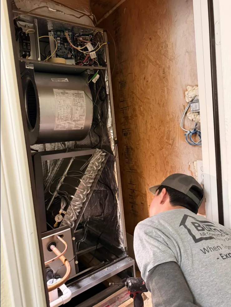 A Burnside Air Conditioning, Heating & Plumbing technician in a branded shirt servicing a home HVAC system in McKinney